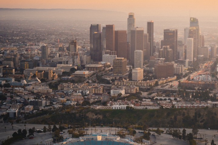 Helicopter over city skyline and stadium at sunset.