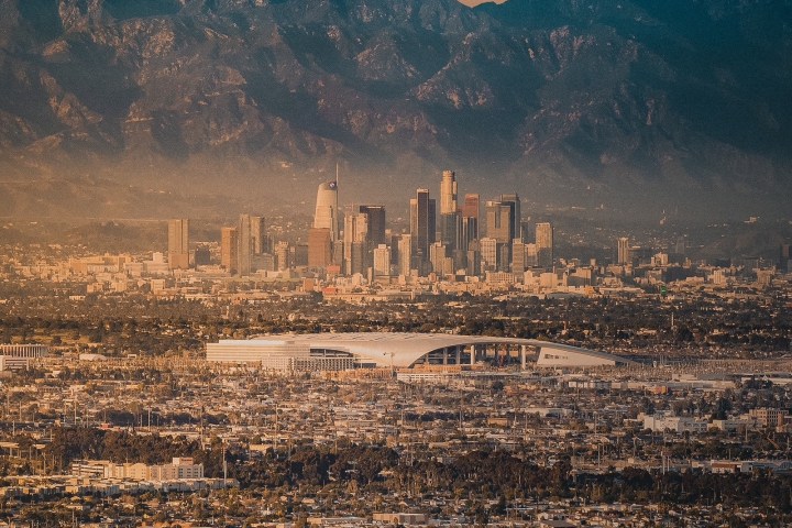 Cityscape at sunset with mountains in the background and skyscrapers in the distance.