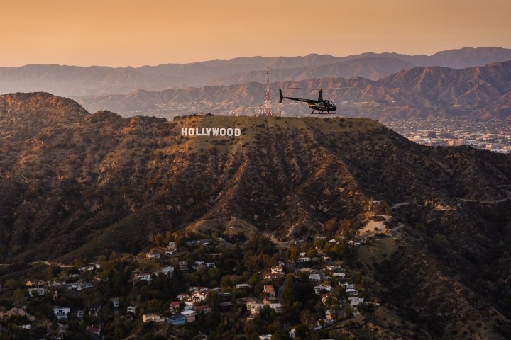 Helicopter flying near Hollywood sign in mountains at sunset.