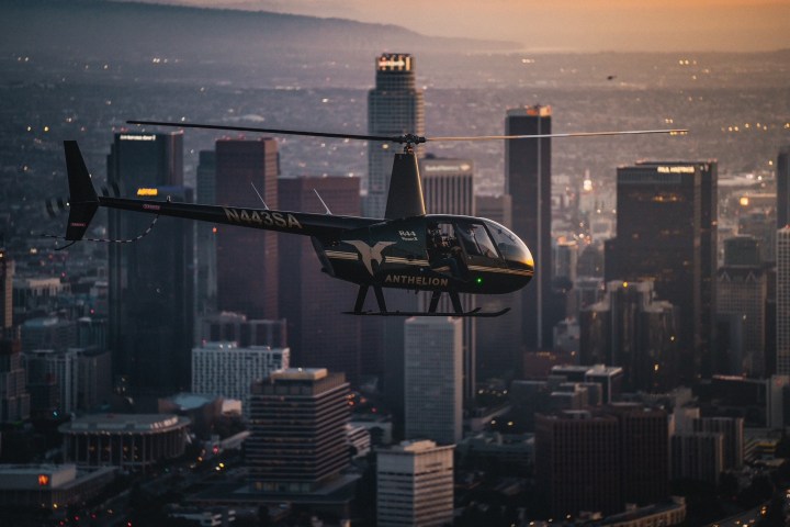 Helicopter flying over a city skyline at sunset with tall buildings visible.