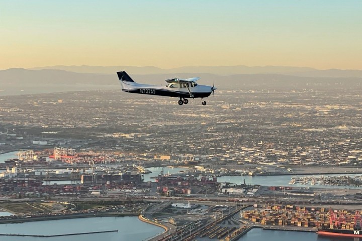 Small airplane flying over a cityscape with water and docks below.