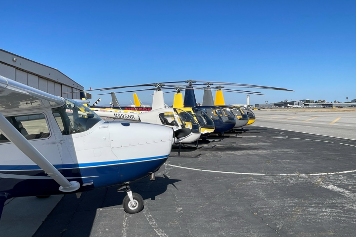Small airplanes and helicopters parked on an airport tarmac.