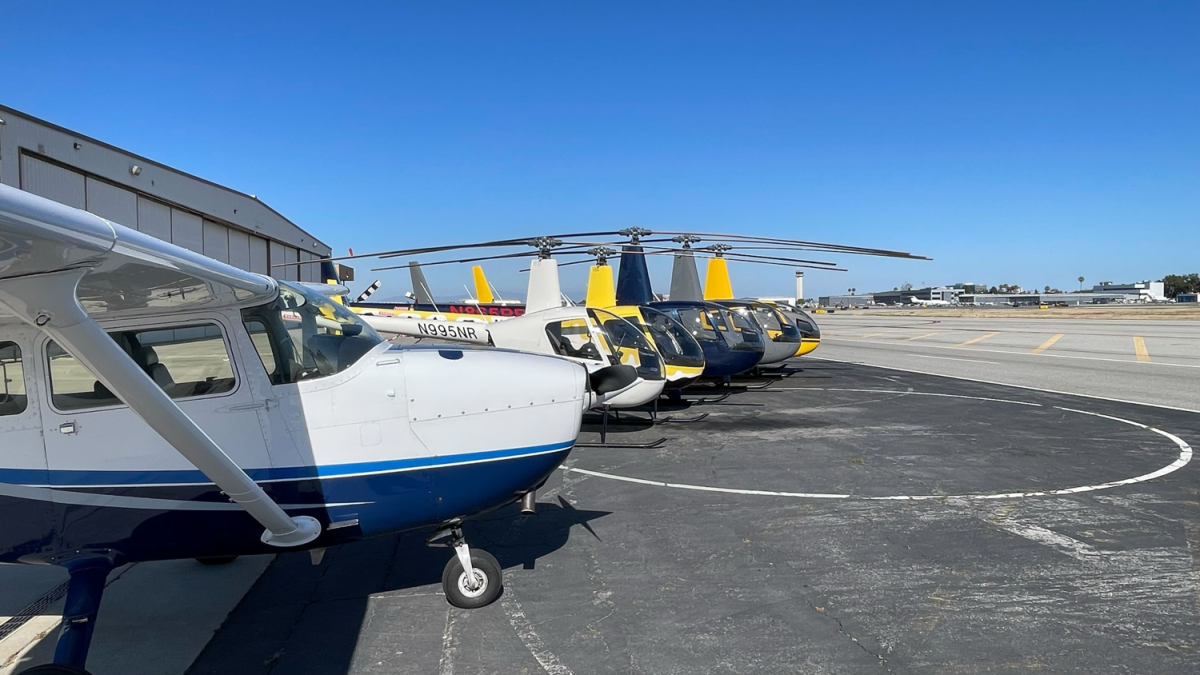 Small airplanes and helicopters parked on an airport tarmac.