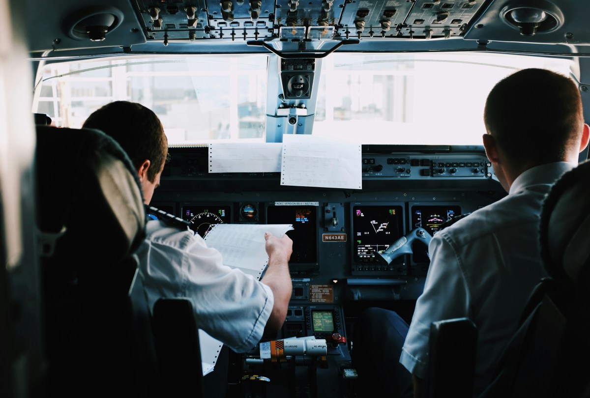 Two pilots in the cockpit of an airplane, reviewing documents and controls.